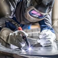 Welding wearing proper helmet and safety accessories working in position 1F.