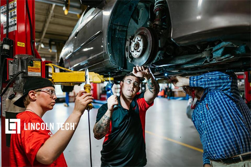 Auto tecnician students working with instructor under a car.